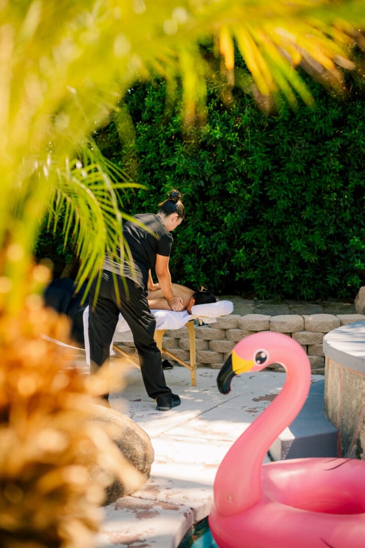 Man preparing a poolside table with food dishes and a flamingo float.